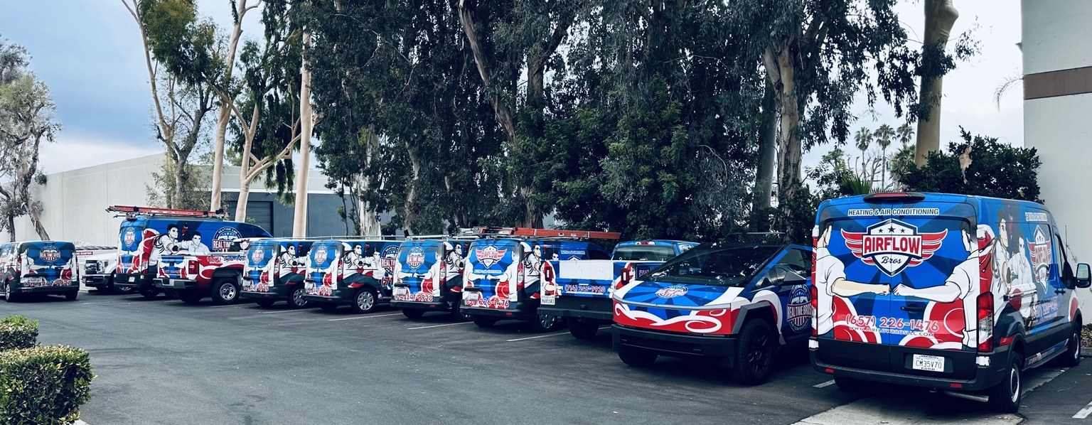 A row of wrapped service vans parked along a tree-lined lot