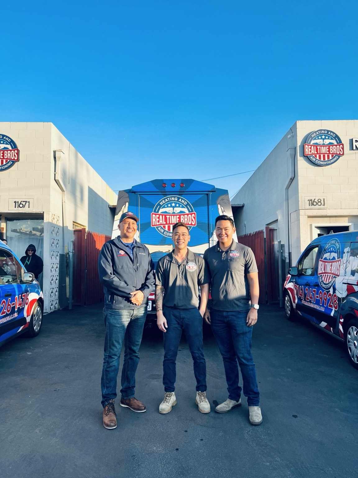 Three team members standing between two wrapped Real Time Bros service vans