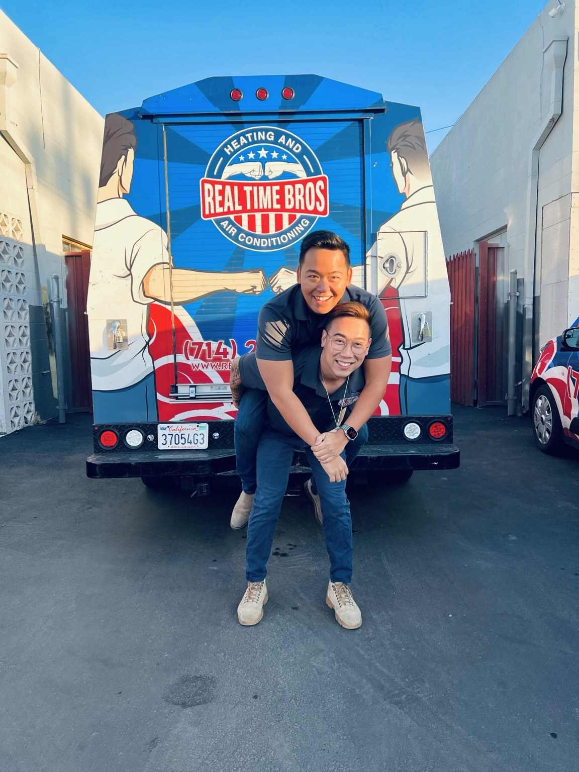Two team members, one carrying the other on his back, in front of a Real Time Bros box truck